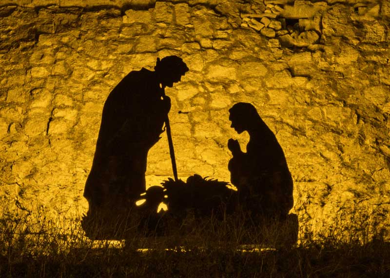 silhouette of a nativity scene against a stone wall